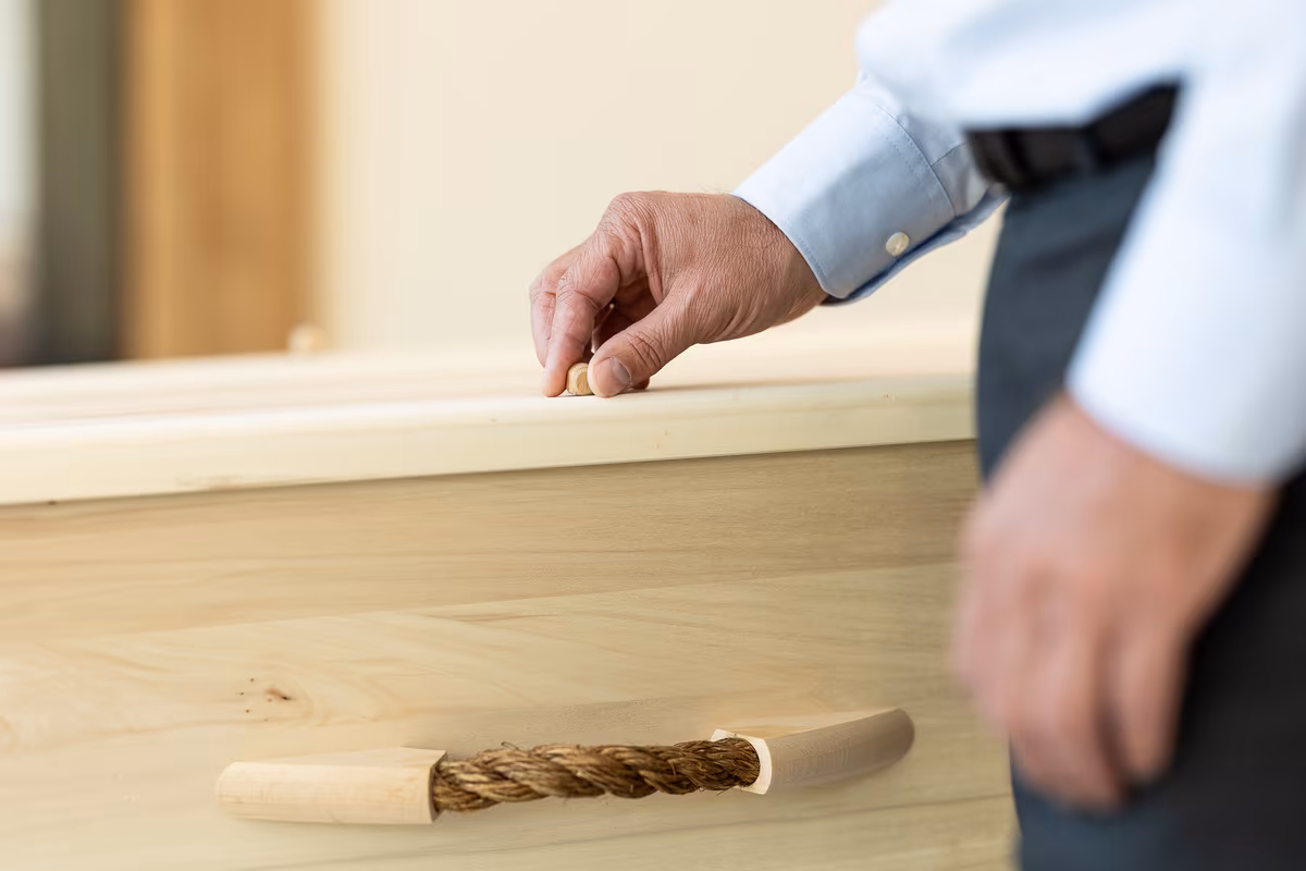 Hand legt symbolisch touw op een houten kist tijdens een begrafenis